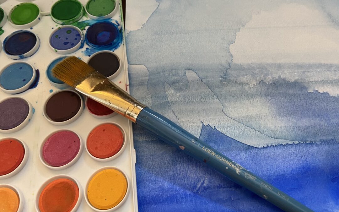 close up view of a watercolor palette, a paint brush, and a blue watercolor painting.