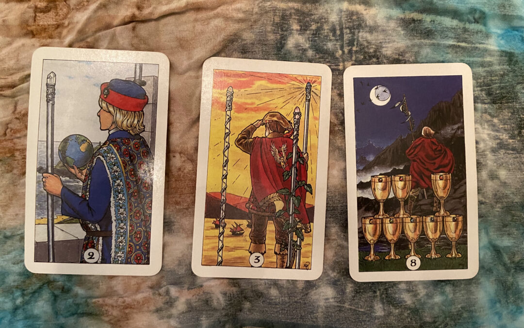 three tarot cards lined up show the 2 of wands, the 3 of wands, and the 8 of cups on a cloth. all cards show a young man with his back to the viewer looking out over the horizon.