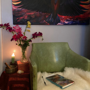 a journal and a pen sitting on a chair with flowers and a lit candle showing a meditative journaling space.