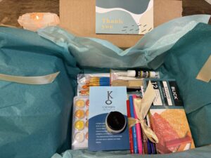Curated Winter Art Therapy Kit with teal tissue paper, gold ribbon, guided prompt cards, art materials, and collage elements arranged for a restorative creative experience.