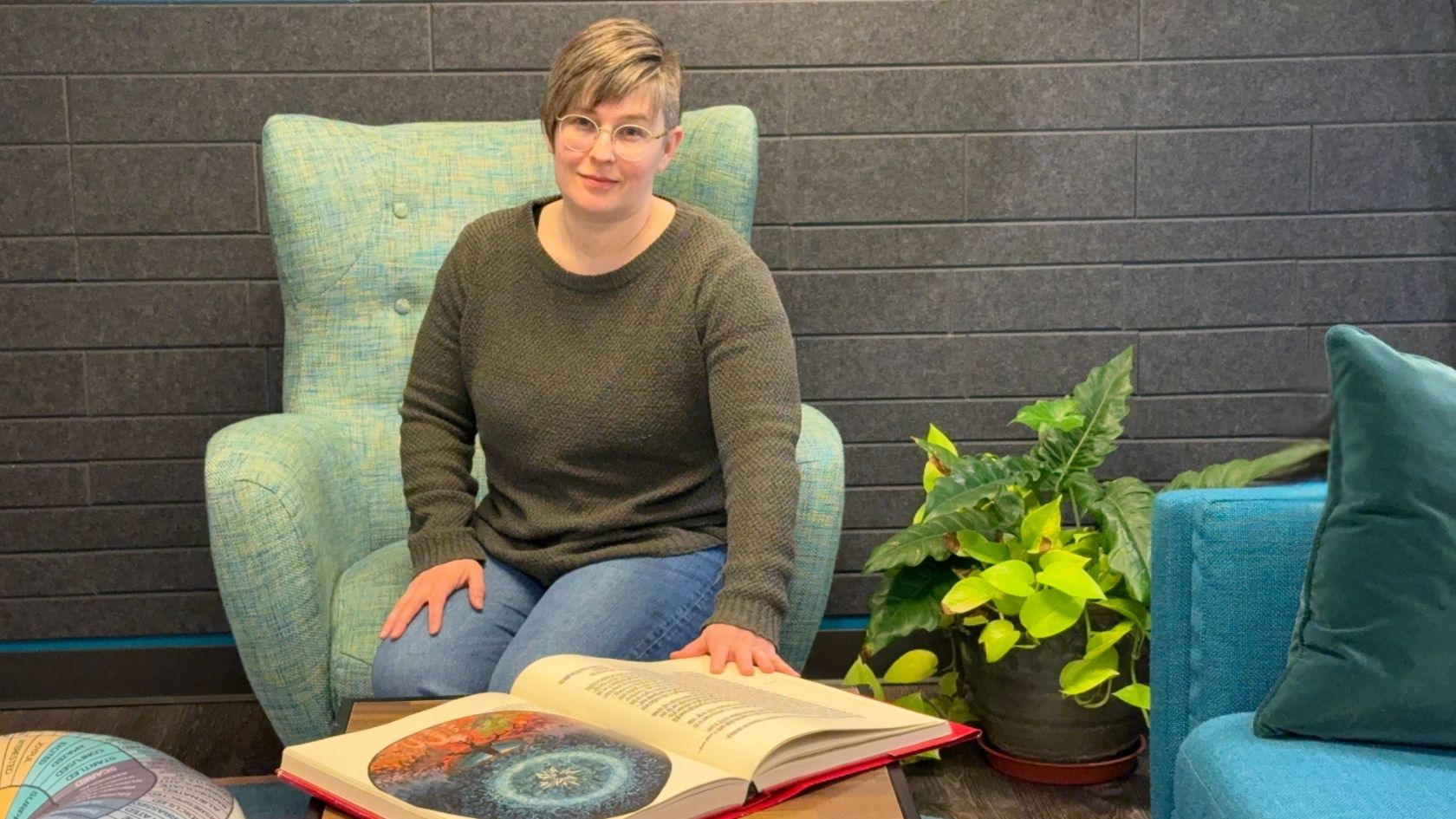 Maggi Colwell, Jungian analyst in training and psychotherapist and art therapist in Columbus, Ohio, seated in her office with a copy of The Red Book by Carl Jung.